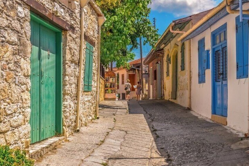 A narrow cobblestone street flanked by buildings with green shutters and a clear sky. 4