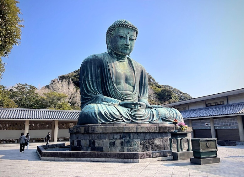 A large seated Buddha statue in a courtyard with a building in the background. 1