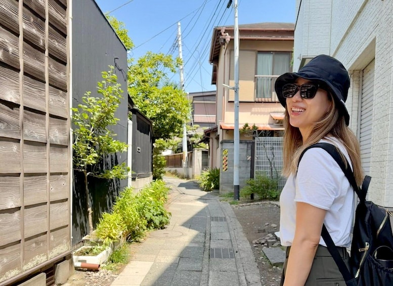 A person standing on a sidewalk next to a wooden fence with greenery and a building in the background. 1