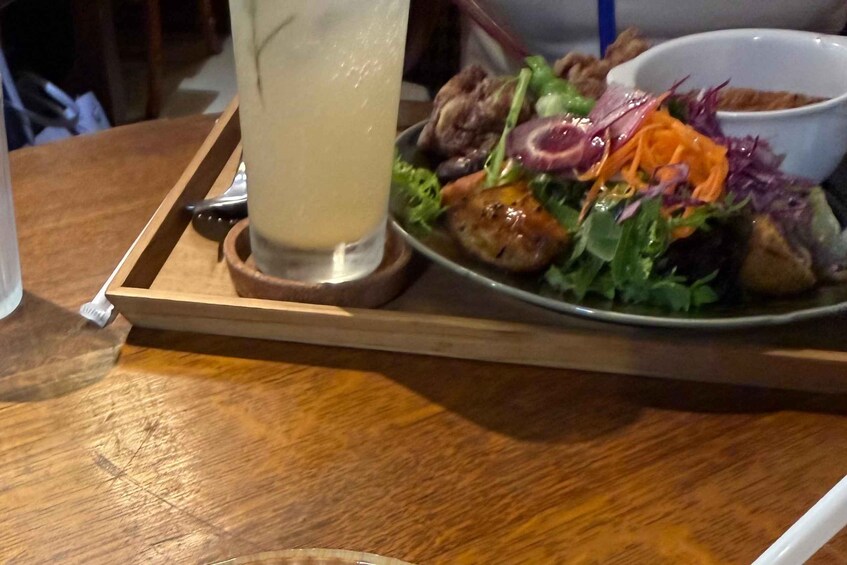 A wooden table with a tray holding a plate of food, a glass of a clear liquid, and a bowl. 5