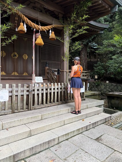 A person standing on stone steps in front of a traditional wooden structure with a rope decoration. 3