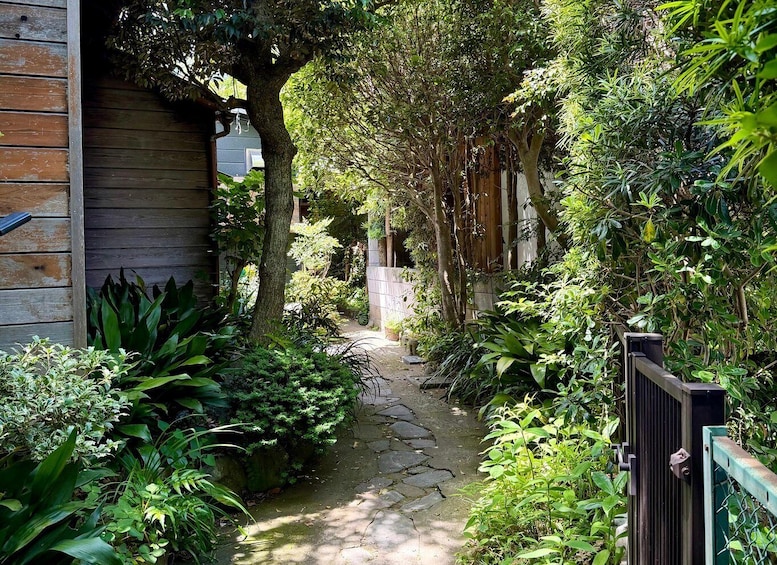 A narrow stone pathway flanked by lush greenery and wooden structures. 3