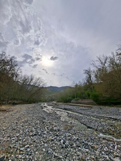 A rocky riverbed with a mountain in the background and a cloudy sky. 3