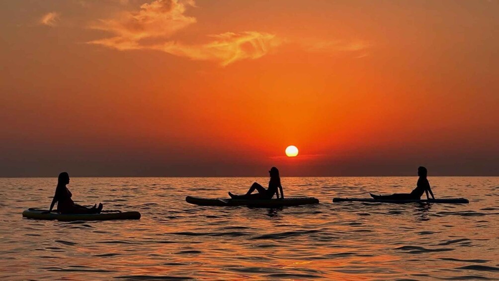 Three people sitting on kayaks on a calm body of water during sunset. 2