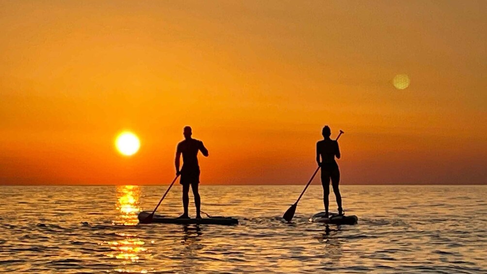 Two people paddleboarding on a calm sea during sunset. 4