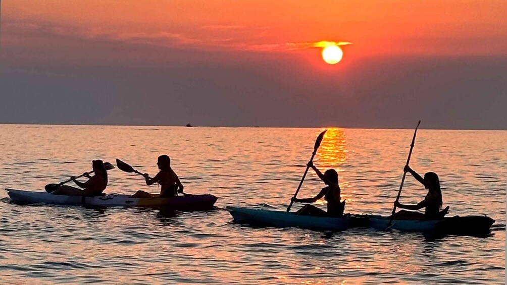 Four people in kayaks on a calm body of water during sunset. 1