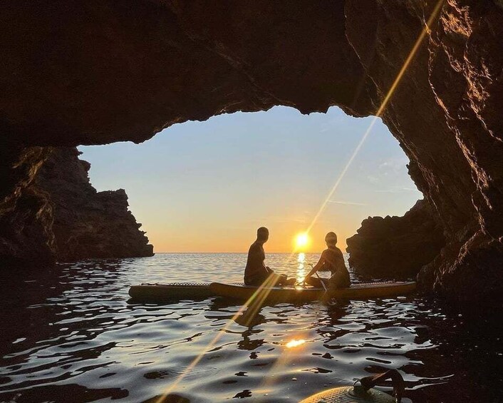 A sunset viewed through a cave opening with two people in a boat. 5