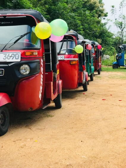 A row of red auto-rickshaws parked on a dirt road with balloons attached to the front. 1