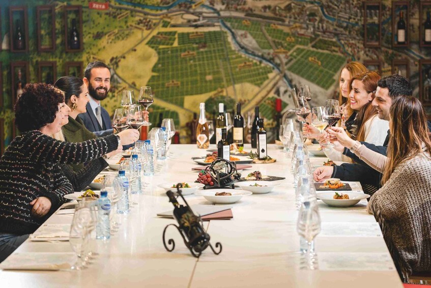 A group of people toasting at a long table with wine glasses and bottles, set against a backdrop of a detailed map. 5