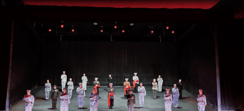 A group of people in uniform on a stage with a dark backdrop and red lighting. 2