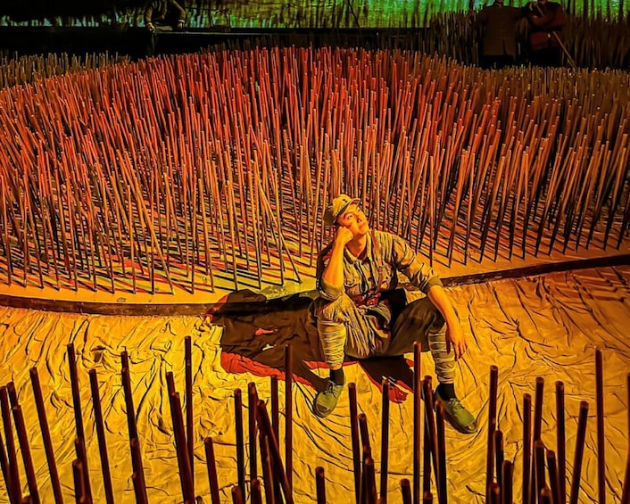 A person sitting on a mat surrounded by numerous bamboo sticks. 4