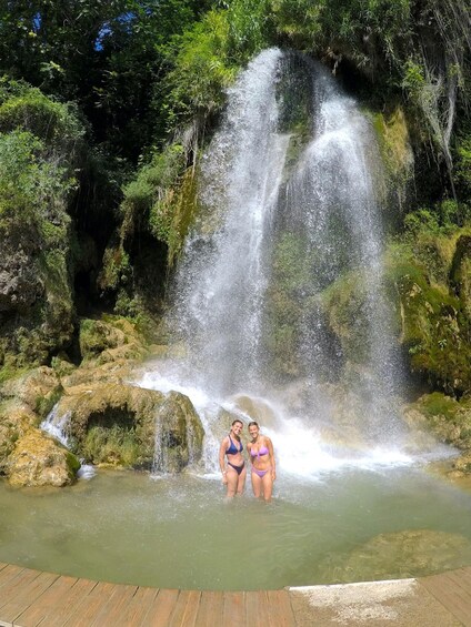 A waterfall with two people standing in a shallow pool at its base. 5