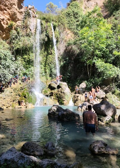 A waterfall cascading into a clear pool surrounded by rocks and greenery. 1