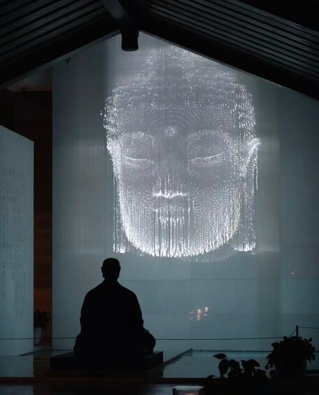 A person sitting in front of a large projection of a face. 3