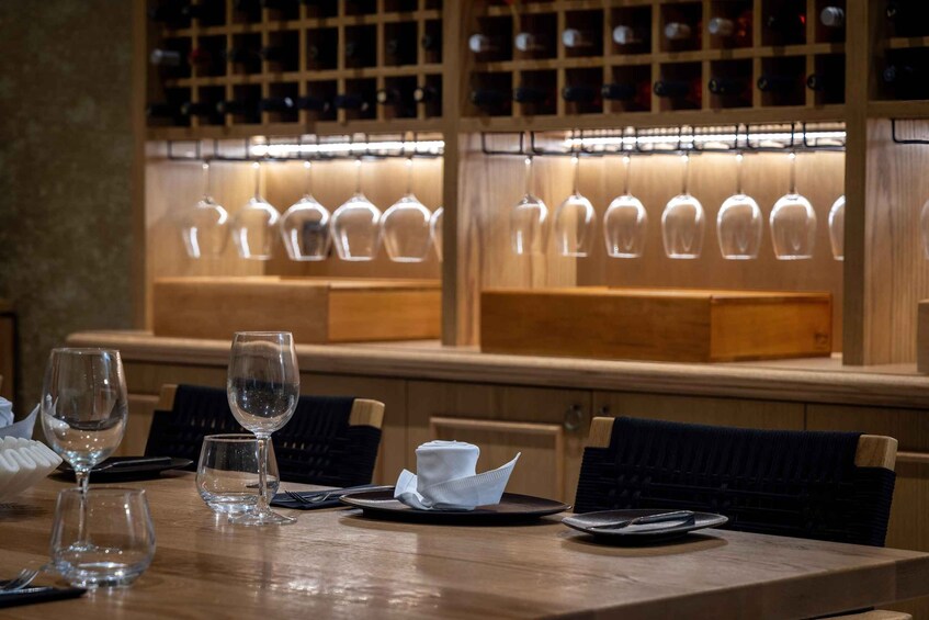 A restaurant interior with a wooden table set for dining, wine glasses, and a wine rack in the background. 1