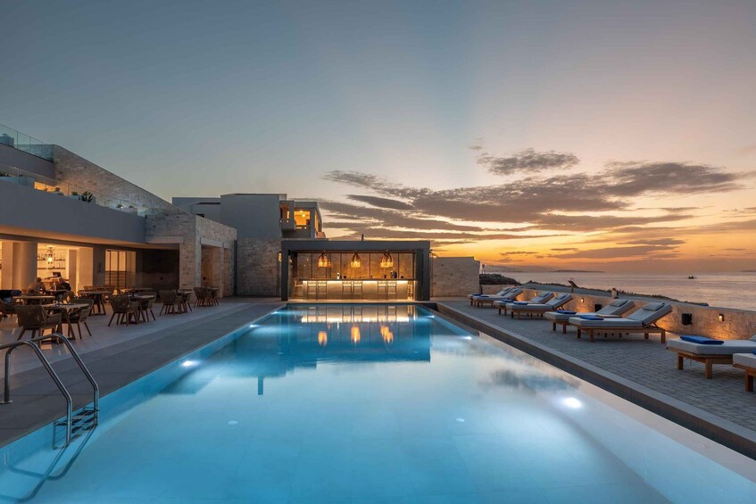 A rooftop pool with lounge chairs and a bar overlooking the ocean at sunset. 5