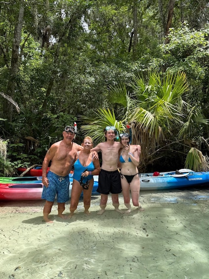 Four people standing on a sandy beach with kayaks and a dense forest in the background. 5