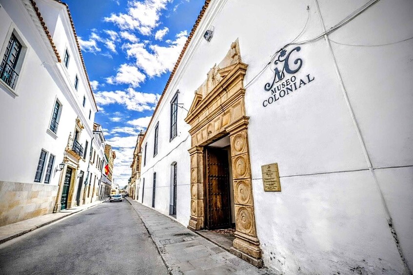 A narrow street with white buildings, a colonial museum sign, and a clear blue sky. 1