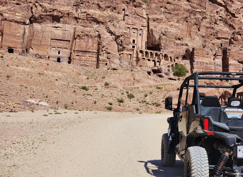 A jeep on a dirt road with ancient rock carvings in the background. 2