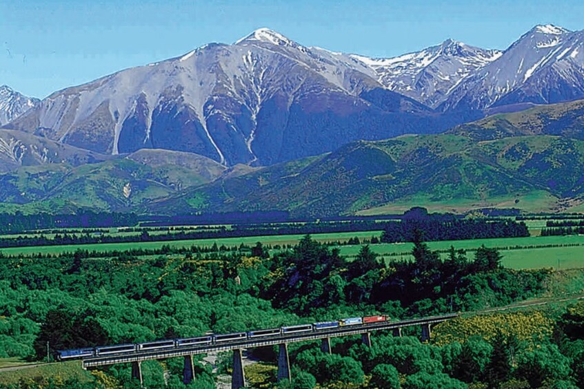 A train on a bridge with mountains in the background. 2