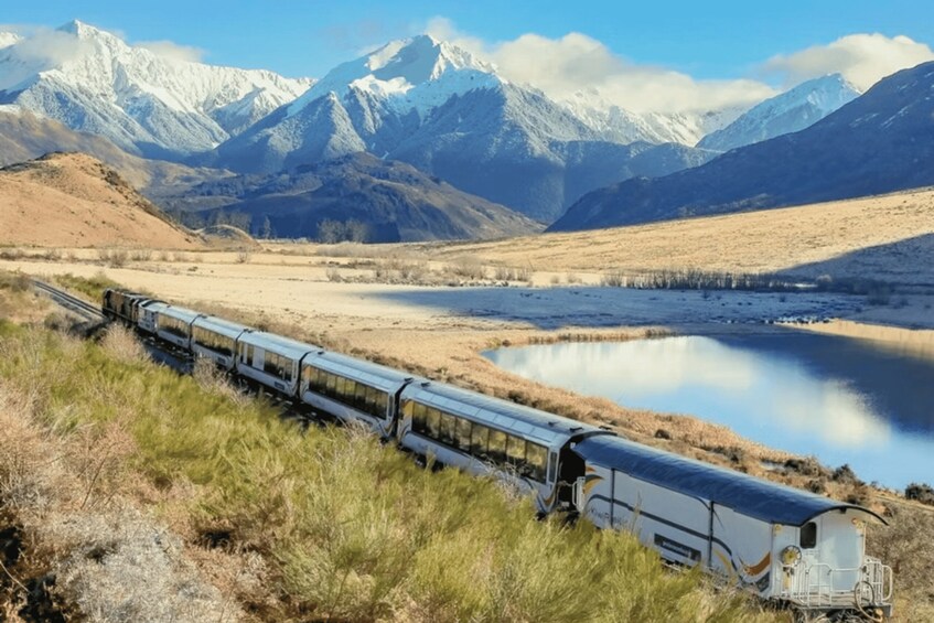 A train traveling through a mountainous landscape with a lake and snow-capped peaks in the background. 1