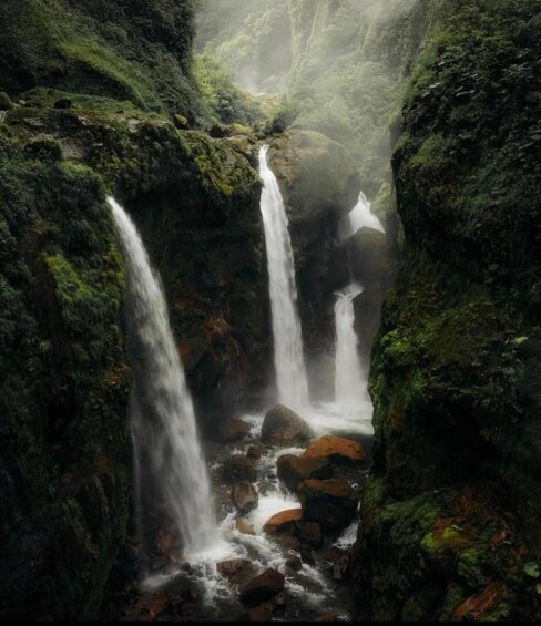 A waterfall cascading through a rocky gorge with moss-covered rocks and dense greenery. 1