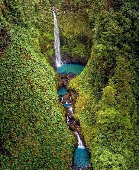A waterfall cascading into a turquoise pool surrounded by lush green forest. 3