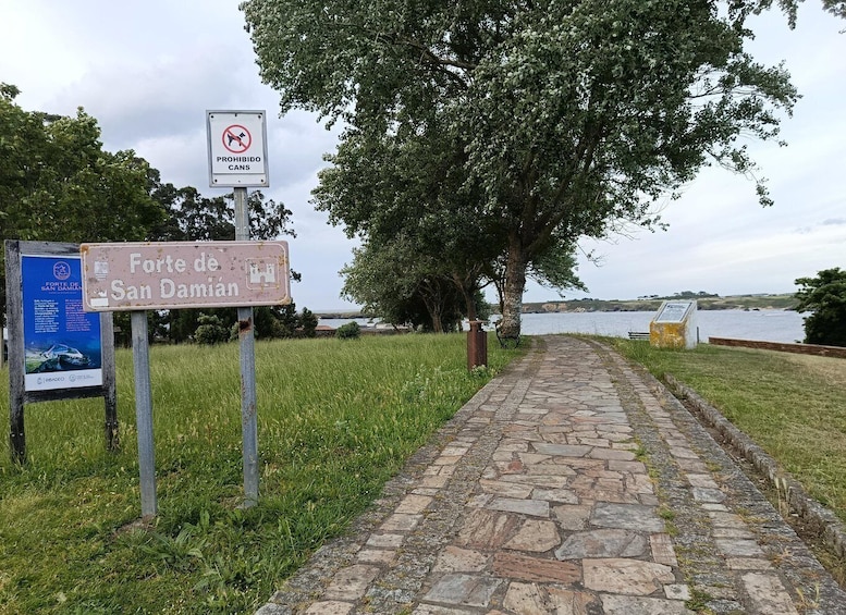 A stone pathway leading to Forte de San Damián, with a 'Prohibido Cans' sign and a blue informational board. 2