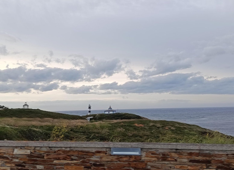A coastal landscape with a stone wall, a gazebo, and two lighthouses. 4