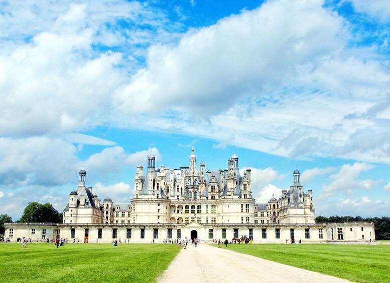 A grand historic palace with multiple towers and domes, surrounded by expansive green lawns and a clear sky. 1