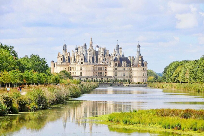 A grand historic building with multiple towers and a river in the foreground. 2