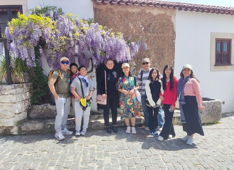 A group of people posing in front of a building with a stone wall and purple flowers. 4