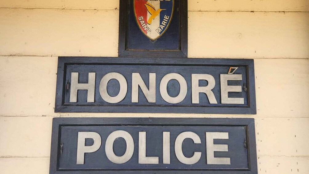 A police station sign with 'HONORE POLICE' on a beige wall. 4