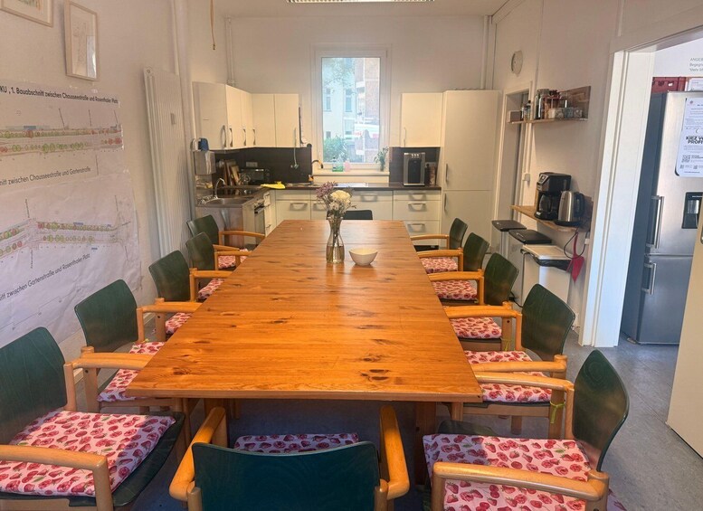 A long wooden table with chairs, a kitchen in the background, and a window. 4