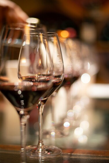 A close-up of a wine glass with a dark liquid, likely red wine, on a bar counter. 1
