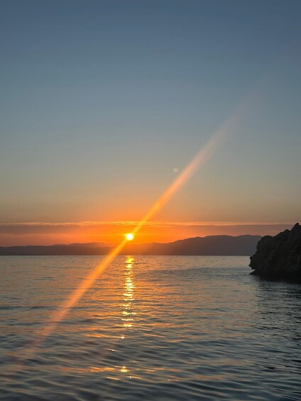 A sunset over a calm sea with a rocky coastline. 3