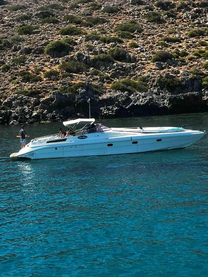 A white speedboat on clear turquoise water with rocky terrain and sparse vegetation in the background. 2