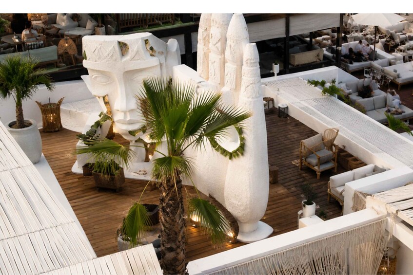 A rooftop lounge with white furniture, palm trees, and a large white sculpture. 3