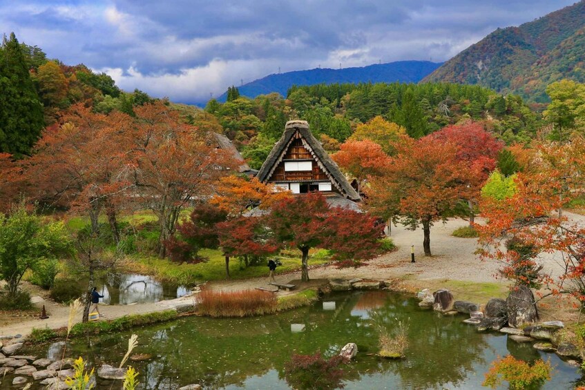A traditional Japanese house surrounded by autumn foliage, a pond, and a mountainous backdrop. 4