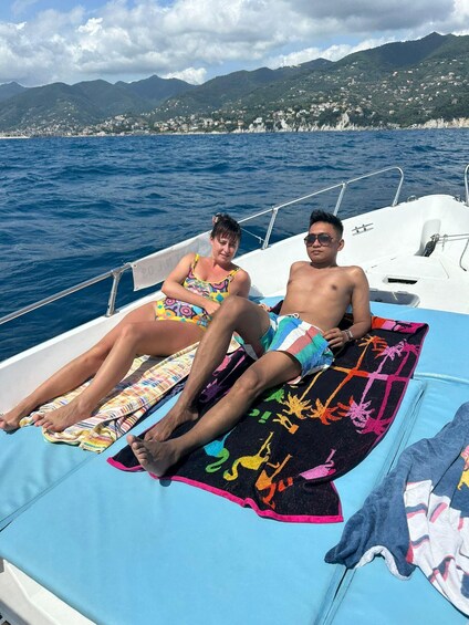 Two people relaxing on a boat with a view of a coastal town and mountains in the background. 4