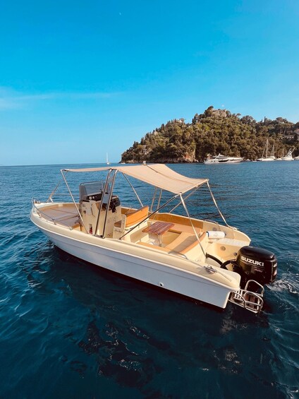 A white motorboat with a canopy, anchored near a rocky coastline with buildings. 5
