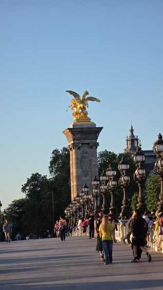 A statue of an eagle atop a column, surrounded by ornate street lamps and a crowd of people. 4