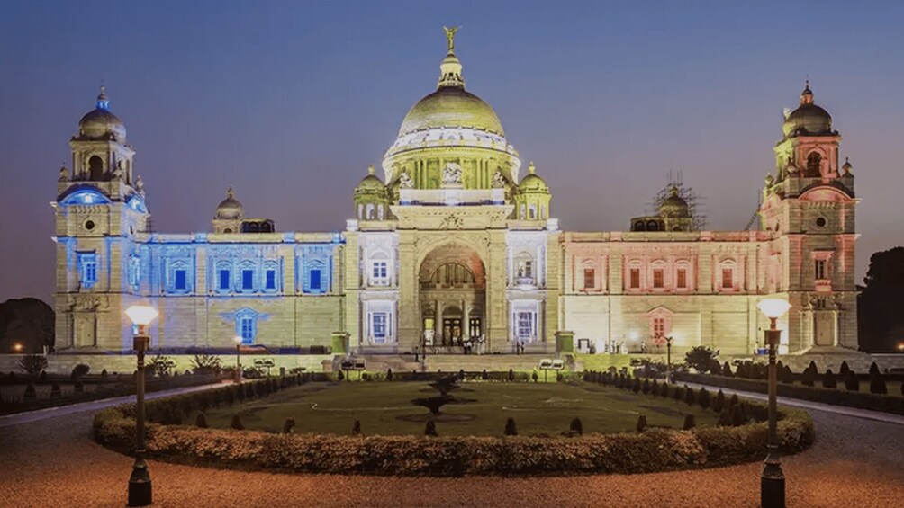 A large, illuminated building with a central dome and two smaller domes on either side, surrounded by a formal garden. 5