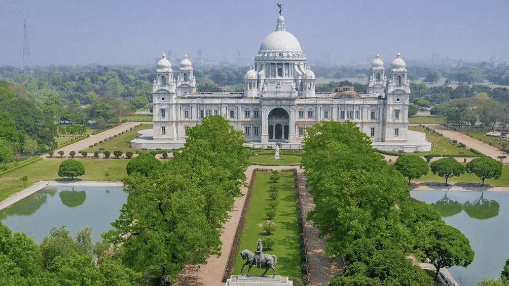 A large, white, domed building with multiple towers, surrounded by lush greenery and water features. 2