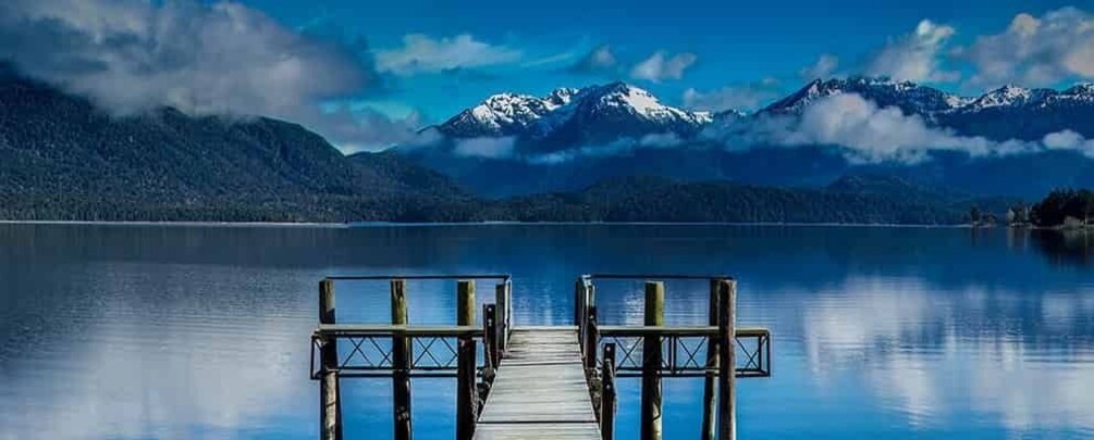 A wooden dock extending into a calm lake with snow-capped mountains in the background. 1