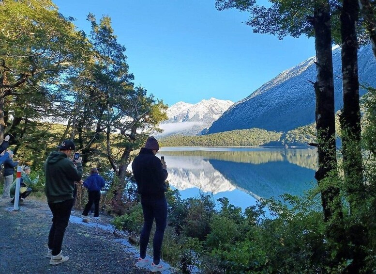 A group of people standing by a lake with mountains in the background. 4