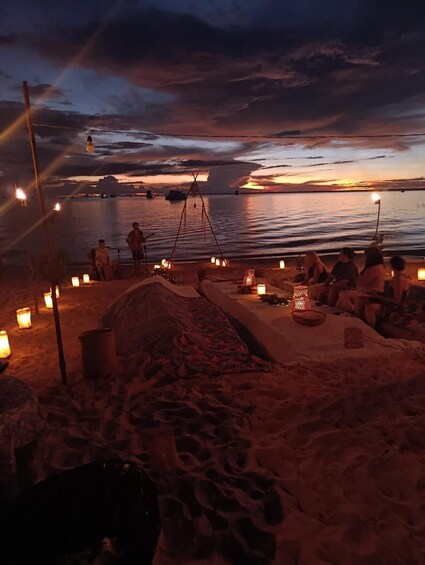 A beach at sunset with people sitting and relaxing, surrounded by sand and candles. 4