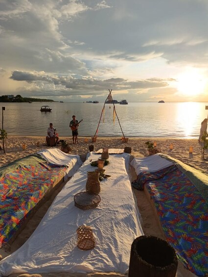 A beach with a row of colorful blankets, a woven basket, and a small structure with hanging items. 3