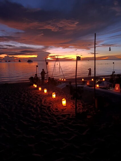 A beach at sunset with people fishing and lanterns on the sand. 5