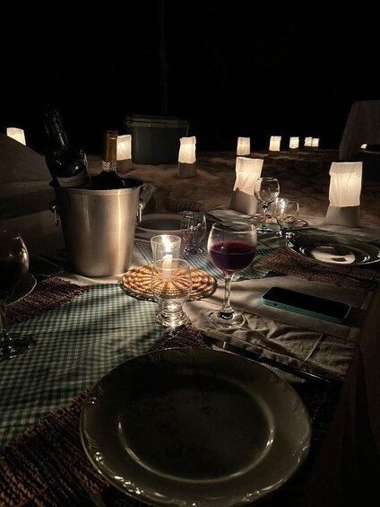 An outdoor dining setup with candles, wine glasses, and a checkered tablecloth. 2